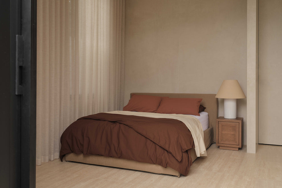 bedroom setting with brown linen bed, white oversized lamp, timber rattan bedside table